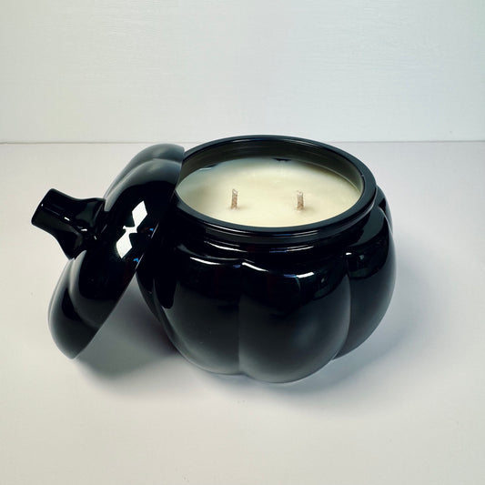 Black pumpkin-shaped candle with a white candle inside on a light gray background