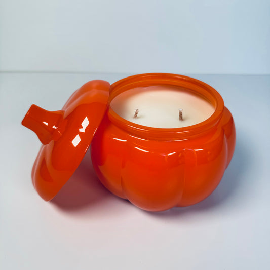 Orange ceramic jar with a lid containing a candle on a light gray background